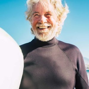 happy mature man with black wetsuit and surfboard at the beach ready to go surf